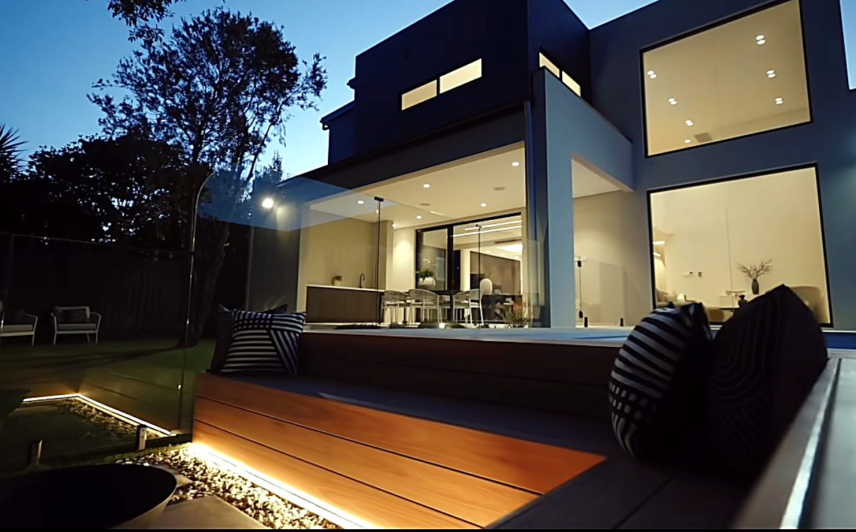 Lit composite deck with built-in bench seating at a modern two-storey home at dusk
